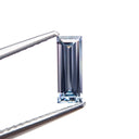 Loose 0.57 ct unheated Madagascar baguette step-cut sapphire held in tweezers against a white background.