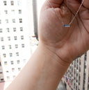 Bar None baguette sapphire necklace in 14K white gold held against a hand, with the faceted bar-link chain and east-west sapphire pendant shown in natural light.