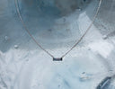 Bar None baguette sapphire necklace in 14K white gold displayed against a water-covered translucent plastic surface.