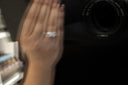 Blurred reflection of a hand wearing a five-stone diamond ring while holding a black notebook, photographed into a mirror with a camera visible in the opposite hand.