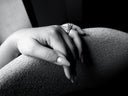 Bespoke ring with a round brilliant cut center diamond, baguette and trapezoid diamonds, worn on a left hand draped over a chair in dramatic black-and-white lighting.