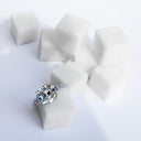 Five-stone diamond ring with an Asscher-cut center photographed among square sugar cubes on a white surface.