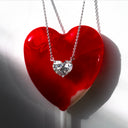 Heart-shaped diamond pendant necklace draped over a cherry-red heart-shaped lollipop on a white surface.